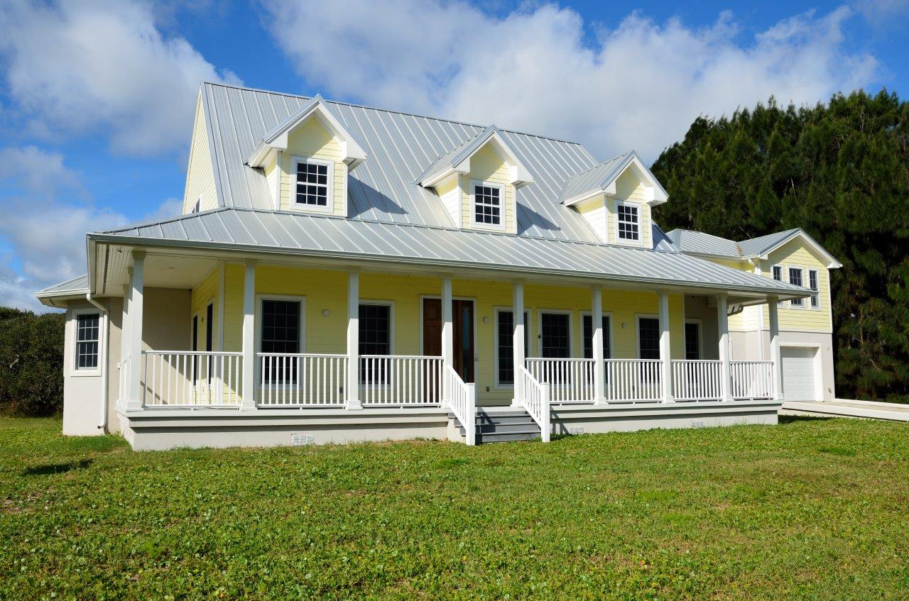 Two-story yellow house with a gray metal roof and a covered porch, showcasing XTEND Contracting’s expertise in exterior remodeling and window installation