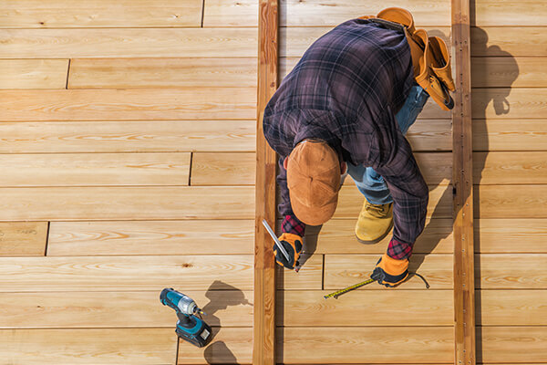 Worker from XTEND Contracting meticulously measuring a wooden plank on a newly constructed deck, symbolizing the precision and dedication in their remodeling services.