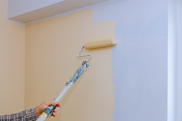 A hand applying light-colored paint to a wall with a roller brush, representing the quality interior painting services provided by XTEND Contracting.
